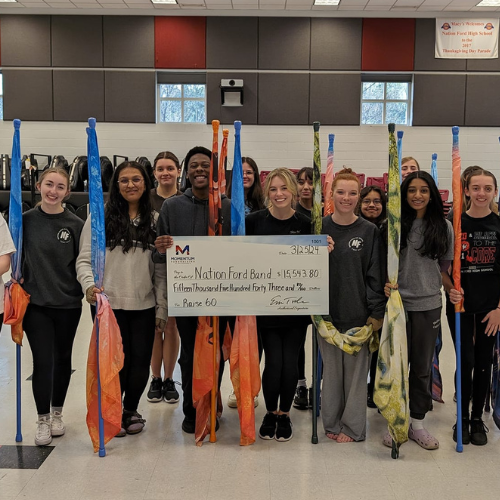 A group of teens with flag poles holds a large check for $15,543.80 made out to Nation Ford Band.